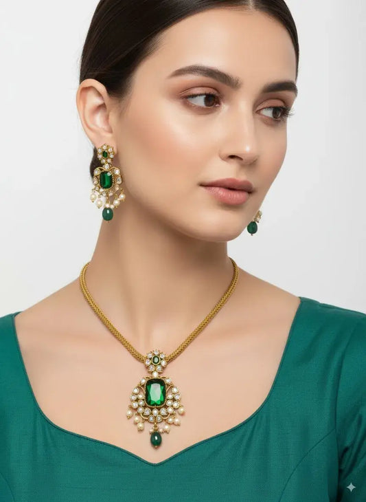 Woman wearing a gold necklace with a green gemstone and matching earrings on a plain background